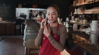 Kırmızı önlüklü genç Asyalı garsonun cep telefonuyla müşterilerle konuşurken orta boy fotokopi çekimleri.