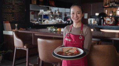 Kameraya poz veren kırmızı önlüklü Asyalı garsonun portresi.