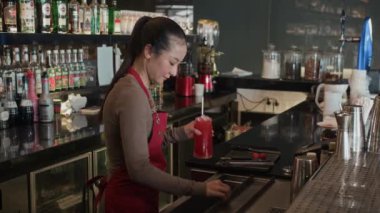 Orta boy, kırmızı üniformalı Asyalı barmenin modaya uygun barda çalışırken misafirlere taze kokteyl hazırlarken.