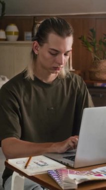 Ev stüdyosunda çalışırken dizüstü bilgisayar kullanan genç moda tasarımcısının dikey görüntüsü.