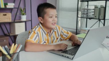 Sınıfta kablosuz dizüstü bilgisayarın önünde otururken internetten ders çalışan Asyalı bir gencin orta boy fotoğrafı.