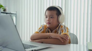 Telsiz bilgisayarda çalışırken kulaklık takan Asyalı bir çocuğun orta boy portresi.
