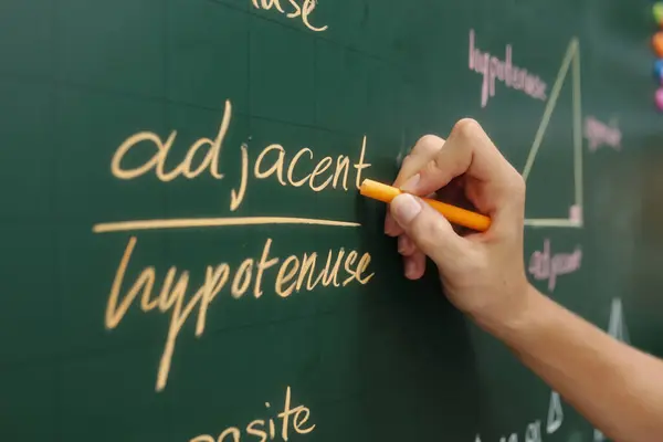 stock image Hand writing mathematical terms on greenboard during teaching session drawing attention to hypotenuse and adjacent with geometric diagram in background