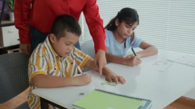 Okul saatlerinde çocukların yazma becerilerini öğrenmelerine yardım eden kadın hoca görüntüsü.