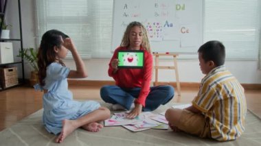 Konuşma terapisi sırasında iki farklı öğrenciye dijital tablet üzerinde eğitici materyaller gösteren İspanyol bayan öğretmenin uzak çekimleri
