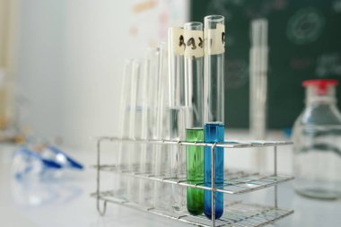 Bilimsel çevrede metal raflara yerleştirilmiş çözümler bulanık arka plan ve diğer laboratuvar ekipmanları görünür.