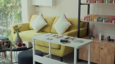 Orta ölçekli modern tırnak sanatları stüdyosu. Masanın yanına yerleştirilmiş sarı kanepe ve manikür salonundaki çeşitli aletler.