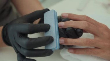 Tanımlanamayan tırnak teknisyeninin eldivenli ellerini kapat. Güzellik stüdyosundaki masada dosyasıyla müşterinin tırnaklarını parlat.