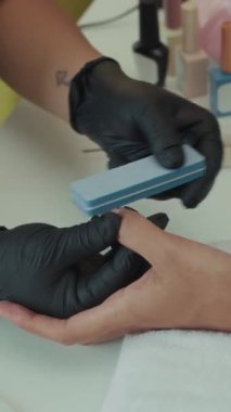 Güzellik stüdyosunda müşterinin tırnaklarını şekillendirmek için dosya kullanan tanınmayan bir uzmanın dikey görüntüsü
