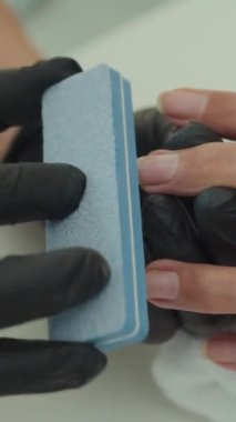 Stüdyoda müşterinin çivilerini şekillendirmek için dosya kullanan isimsiz manikürcünün dikey görüntüsü.