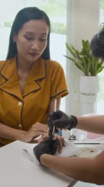 Güzellik stüdyosunda genç Asyalı kadına manikür yapan bir uzman dikey çekimi.