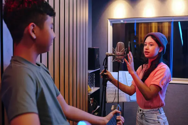 stock image Girl and boy recording song in music studio while using microphone and guitar for acoustic performance, boy holding guitar and girl singing into microphone, recording session for music production