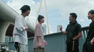 Sokak kıyafetleri içindeki bir grup gencin şehir arka planına karşı havadan sudan konuşmalarının düşük açılı görüntüsü