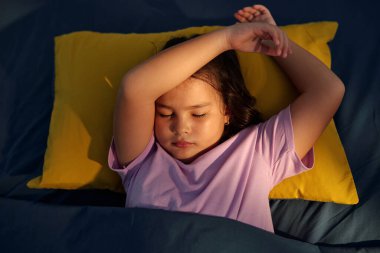 Yatak odasında uyuyan küçük kızın yüksek açılı görüntüsü.