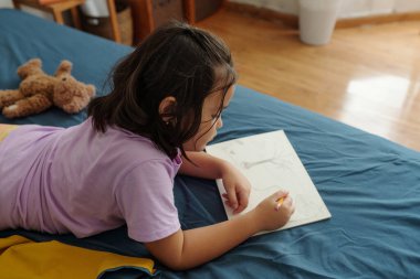 Çizim defterinde resim çizen küçük kızın yüksek açılı görüntüsü odada kalemle.