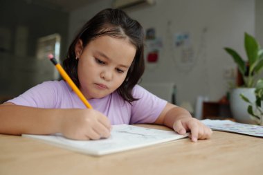 Masada oturan ve kalemle resim çizen kız.