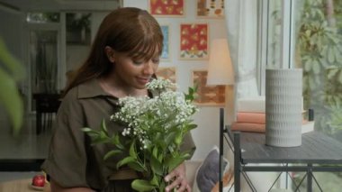 Evdeki vazoda çiçeklerle süslenmiş orta boy siyah kadın resmi.