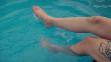 Tanımlanamayan bir kadın dövmesi var. Bacaklarını yüzme havuzuna daldırıyor.