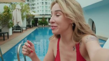 Kafkas kökenli genç bayan turistin, yaz tatilinde yüzme havuzu hakkında kameraya konuşurken ki görüntüsü.