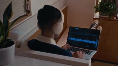 Kablosuz kulaklıklı bir adamın ses dalgalarını analiz edişine ve ses düzenleme ve karıştırma üzerine odaklanırken kapalı alanda kablosuz dizüstü bilgisayar kullanarak müzik prodüksiyonu üzerinde çalışmasına