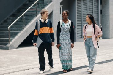 Bir grup öğrenci kampüs boyunca birlikte yürür ve çalışmalarını tartışırlar.