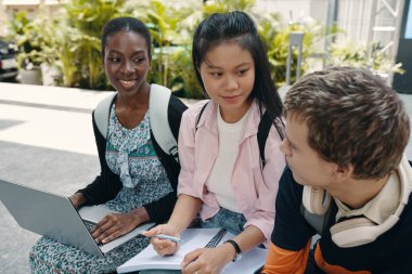 Bir grup öğrenci dışarıda oturuyor ve takım halinde dizüstü bilgisayarda çalışıyorlar.