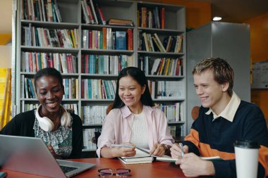 Bir grup öğrenci kütüphanede çalışırken dizüstü bilgisayarda konferans yapıyorlar.