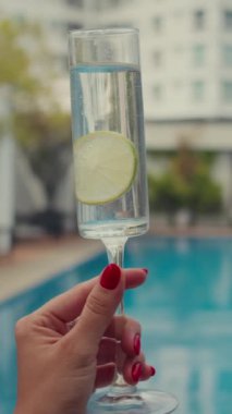 Havuz kenarında limonlu içki bardağı tutan kimliği belirsiz bir kadının görüntüsü dikey zum.