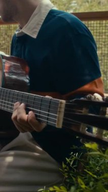 Erkek müzisyenin dışarıda akustik gitar çalarkenki dikey çekimi.