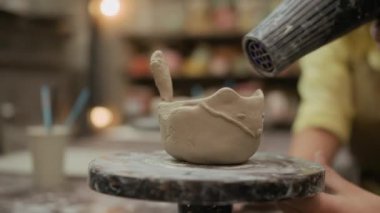 Tanımlanamayan birinin ellerini kapayarak atölyedeki çömlek çarkında dekoru olan kil kaseyi üflüyorlar.