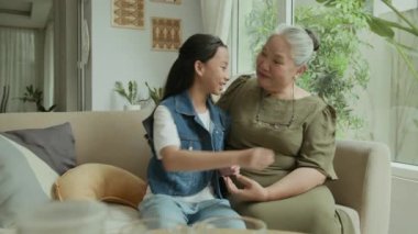 Orta boy Asyalı genç bir kızın evde kanepede otururken büyükannesine sarılıp uyuduğu bir fotoğraf.