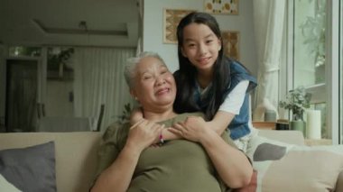 Oturma odasında genç torununa sarılan Asyalı bir kadının orta boy portresi.