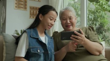 Yaşlı Asyalı kadın ve torununun kapalı alanda videolar izlediği düşük açı.