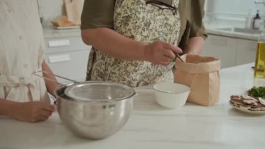 Ev mutfağında birlikte yemek pişirirken unları elleyen tanınmamış insanların kırpılmış fotoğrafları.