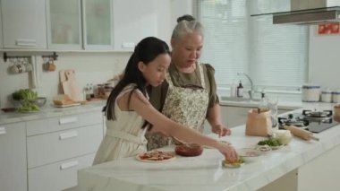 Orta boy Asyalı büyükannenin evde torunuyla pizza pişirmesi.