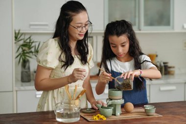 Anne kızına mutfakta bitki çayı yapmayı öğretiyor.