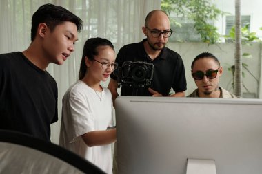 Bir grup insan bilgisayar monitörüne bakıyor ve takımda çekim yapmayı tartışıyorlar.