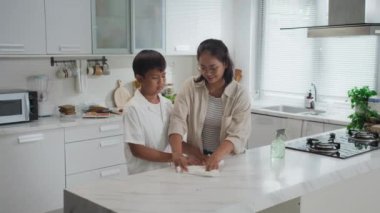Geniş açı Asyalı anne rehberliği yapıyor genç oğlu mutfak tezgahında temizlik yapıyor.