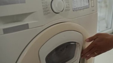 Anonim kişinin evde çamaşır makinesi döngüsü kurarken görüntüsü kesilmiş.