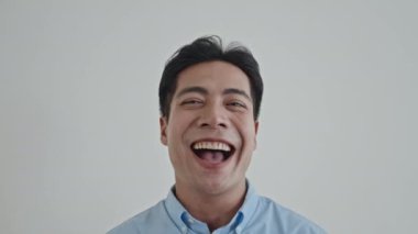 Beyaz arka planda izole edilmiş, gülen ve kameraya bakan kendine güvenen Asyalı adamın yakın portresi.