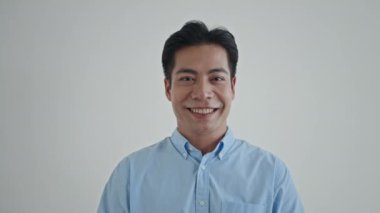 Beyaz arka planda izole bir şekilde poz verirken kameraya öpüşen Asyalı bir gencin orta boy portresi