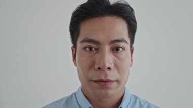 Beyaz arka planda poz verirken sürpriz duygular gösteren Asyalı erkek modelin yakın plan portresi