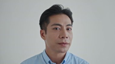 Yüzünde beyaz bir gülümsemeyle kameraya dönen neşeli Asyalı adamın yakın portresi.