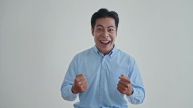 Mavi gömlekli karizmatik Asyalı adamın orta boy portresi beyaz arka planda büyük bir sevinç yaşıyor.