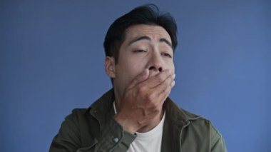 Mavi arka planda esneyen yorgun Asyalı adamın orta boy yakın çekimi, boşluğu kopyala