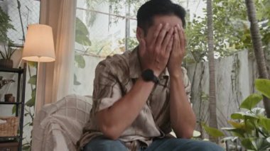 Oturma odasındaki koltukta otururken sorunlarından muzdarip depresif Asyalı erkek milenyuma düşük açılı bakış açısı