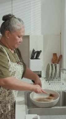 Yaşlı Asyalı kadının fırça kullanırken evdeki mutfak lavabosunu tek tek temizlerken dikey pozu.