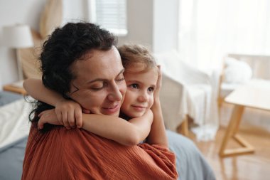 Little girl embracing her mother while they resting in the room clipart