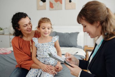 Sosyal hizmetler görevlisi evde anne ve kızıyla konuşurken not alıyor.