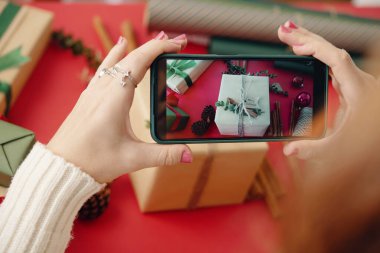 Güzel paketlenmiş bayram hediyelerini akıllı telefonla çeken, yaratıcılık ve şenlik ruhu sergileyen biri. Çam kozalakları ve süsler tatil atmosferini artırır